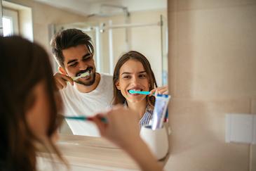 man and woman brushing their teeth
