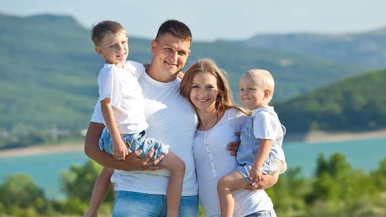 Mom, dad, and two young sons smiling near a lake