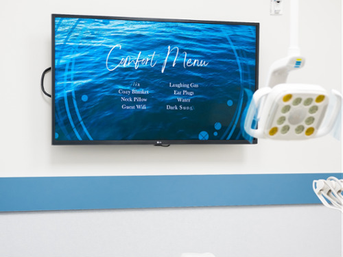 A modern dental treatment room featuring a wall-mounted flat-screen television to help patients relax during procedures.